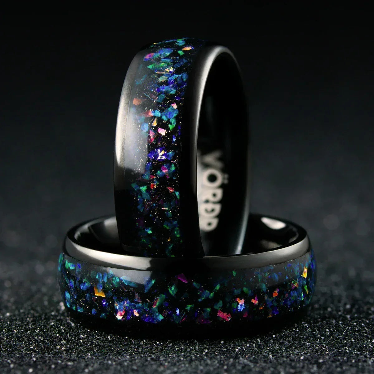 Anillo negro con incrustaciones brillantes multicolor sobre fondo oscuro, joyería moderna.