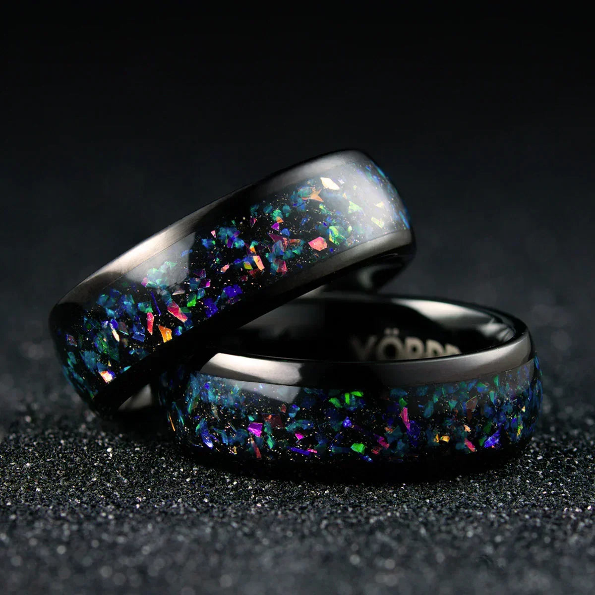 Anillos negros con incrustaciones iridiscentes y textura brillante sobre fondo oscuro.