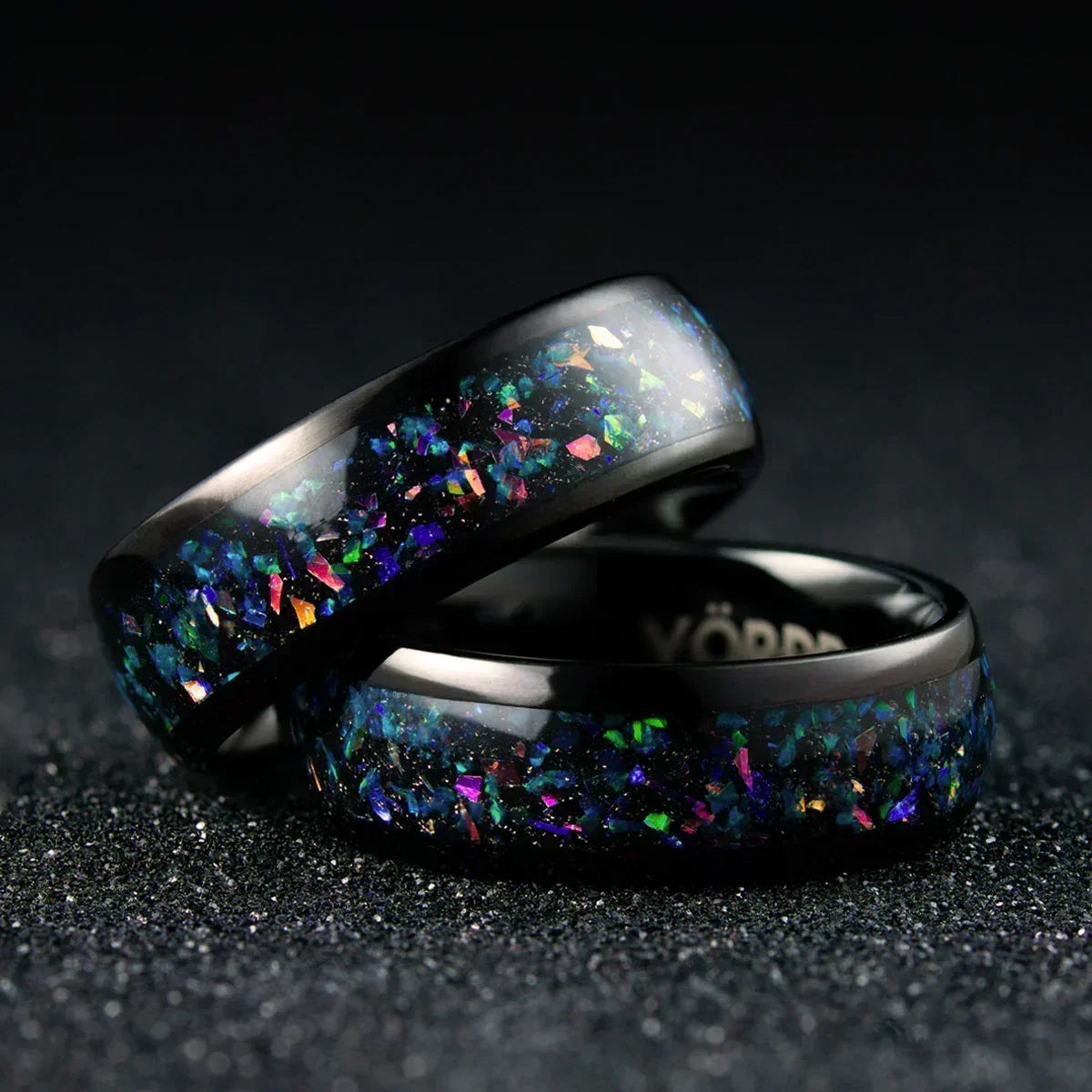Anillos negros con incrustaciones iridiscentes y textura brillante sobre fondo oscuro.