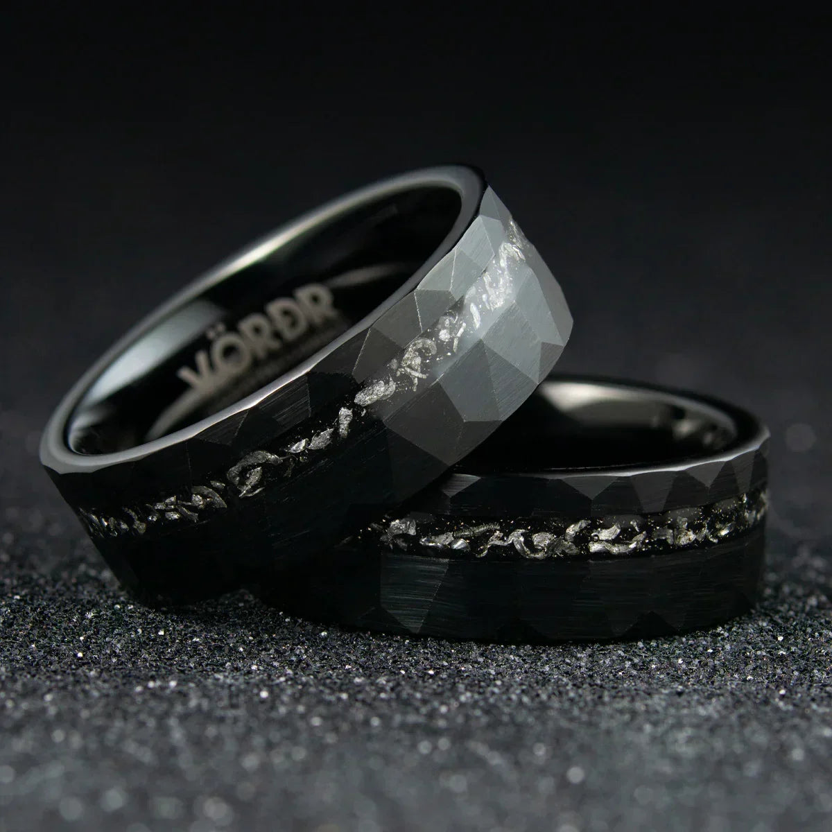 Anillos negros facetados con incrustaciones metálicas brillantes sobre fondo oscuro
