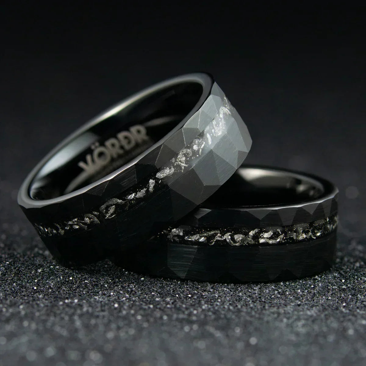 Anillos negros facetados con incrustaciones metálicas brillantes sobre fondo oscuro