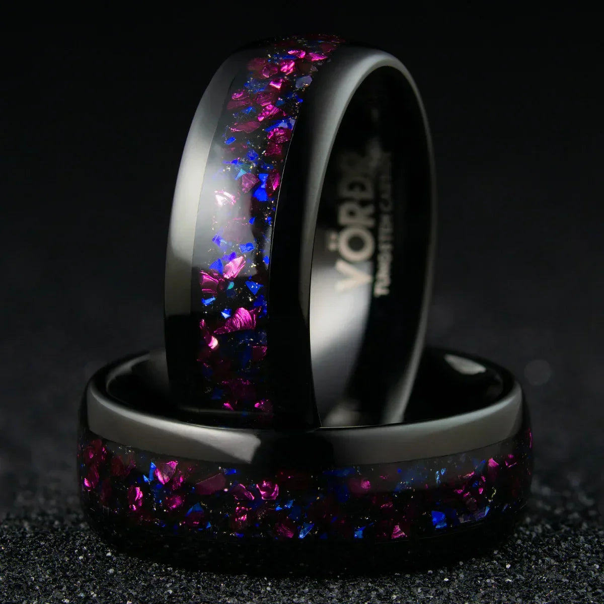 Anillo negro con incrustaciones brillantes púrpura y azul, sobre fondo oscuro, joyería moderna.