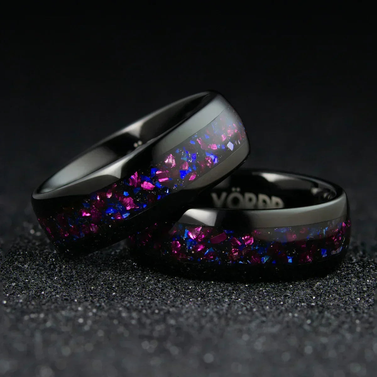 Anillos negros con incrustaciones brillantes en tonos violeta y azul sobre fondo oscuro