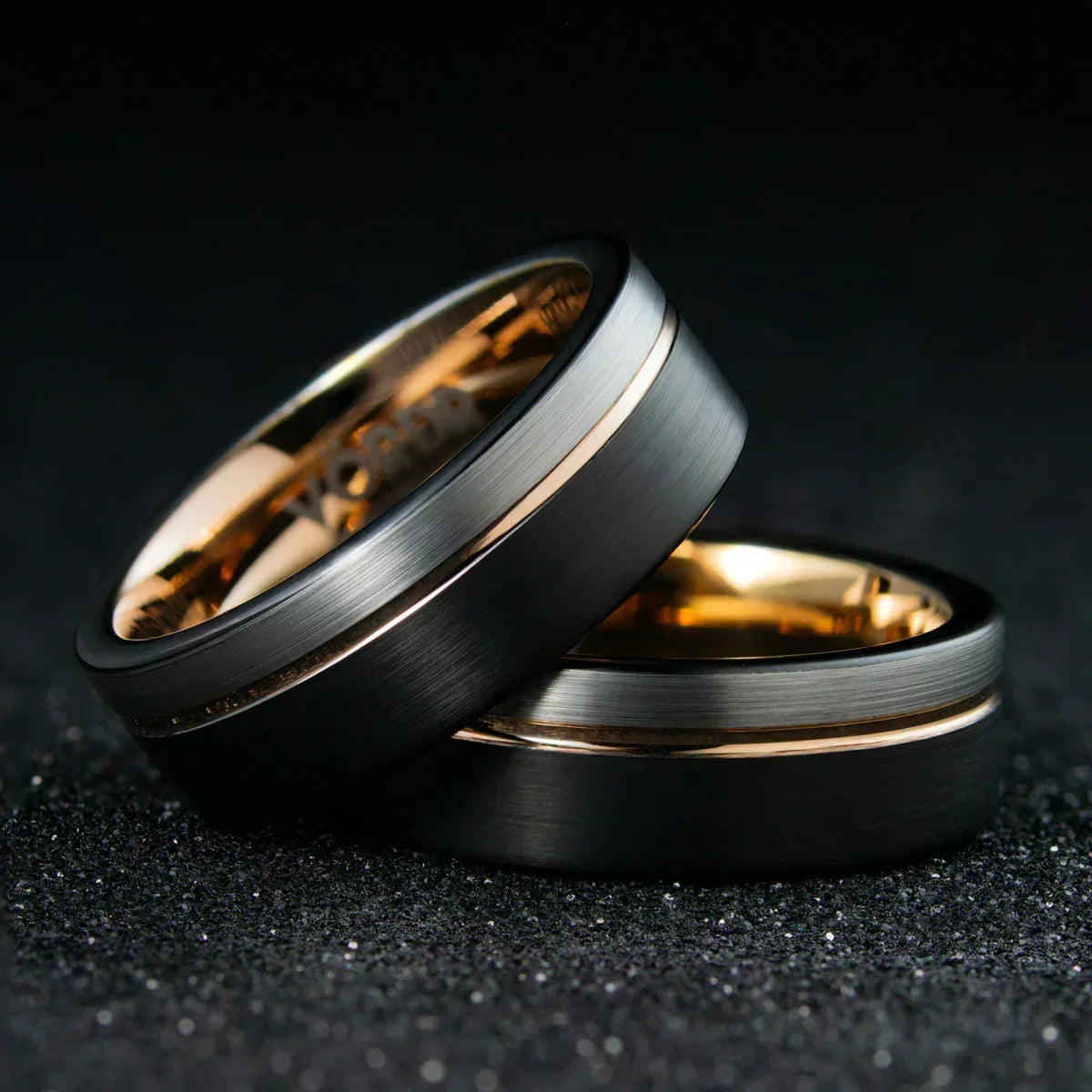 Anillos de matrimonio de tungsteno negro con detalles en oro sobre fondo oscuro