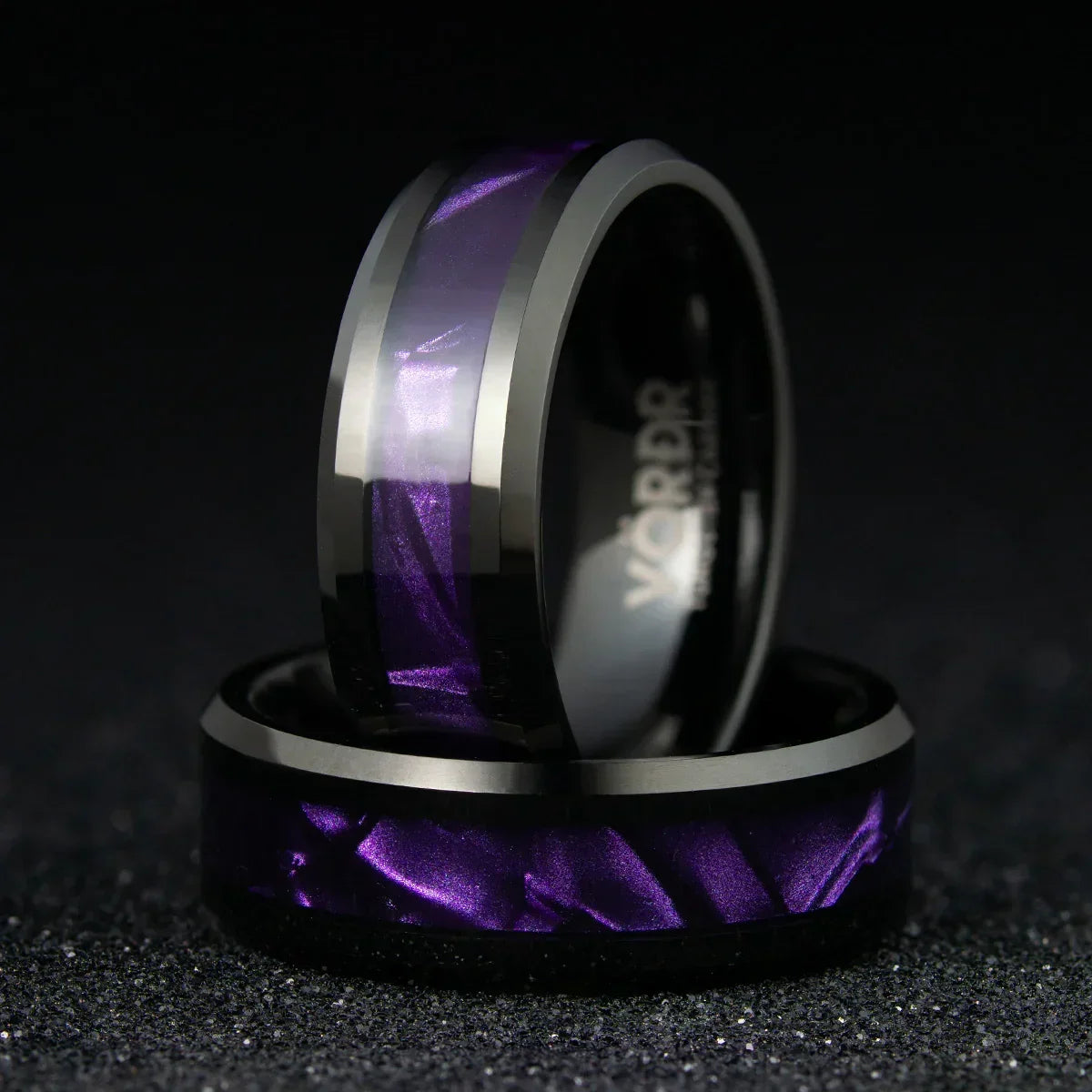 Anillos modernos de acero inoxidable con incrustación púrpura metálica sobre fondo negro.