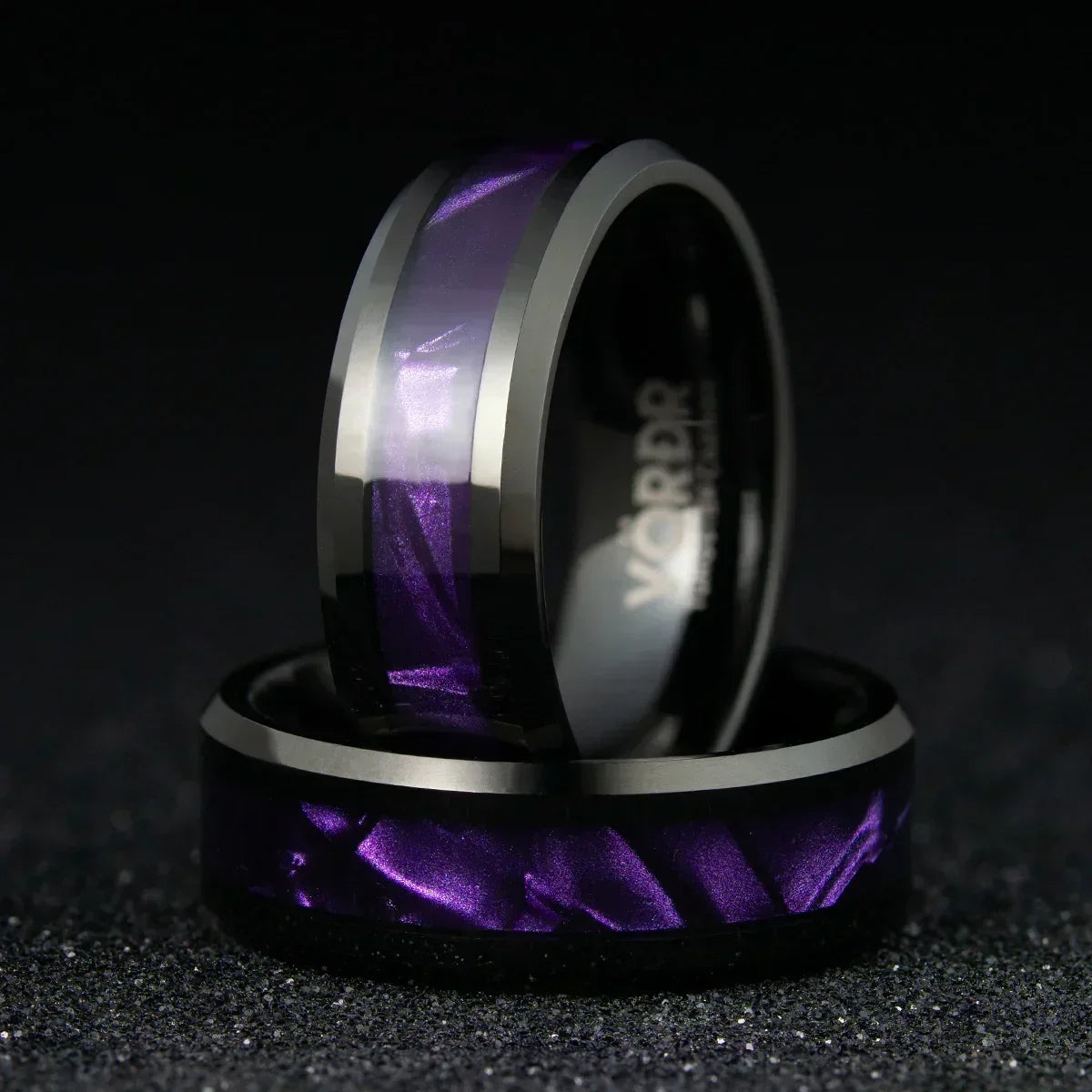 Anillos modernos de acero inoxidable con incrustación púrpura metálica sobre fondo negro.