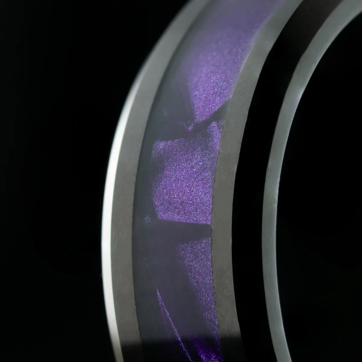 anillo de acero con franja interna púrpura sobre fondo negro, vista macro