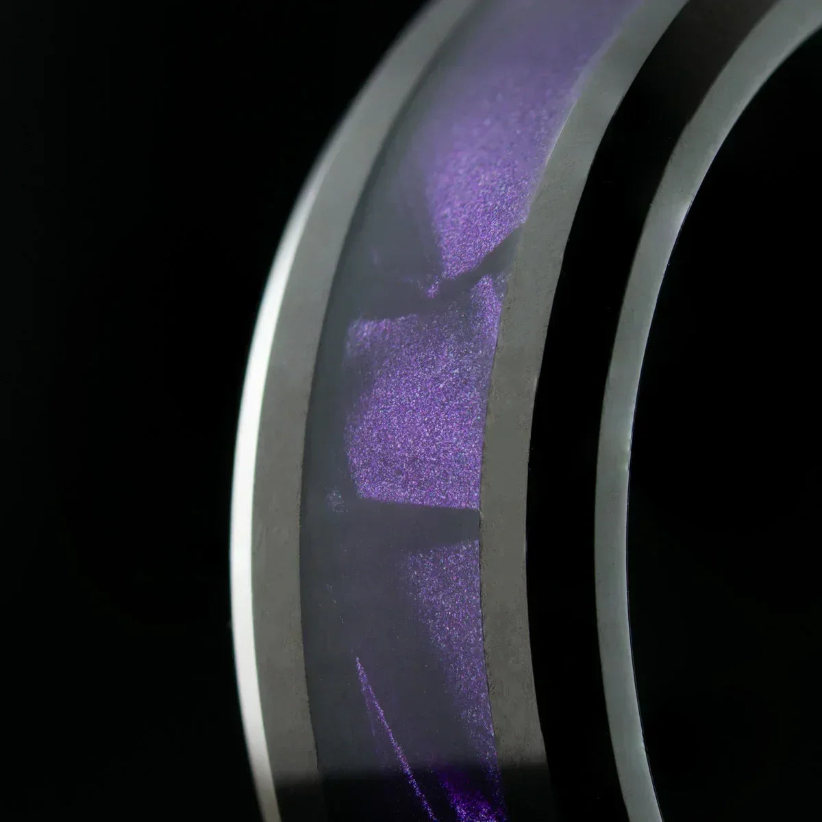 anillo de acero con franja interna púrpura sobre fondo negro, vista macro