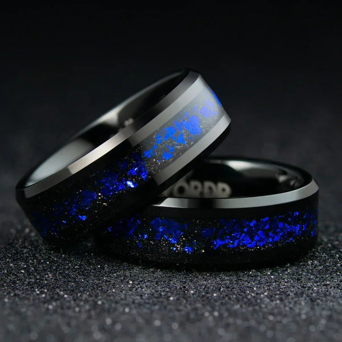 Anillo negro con incrustaciones azules brillantes sobre fondo oscuro, joyería moderna.
