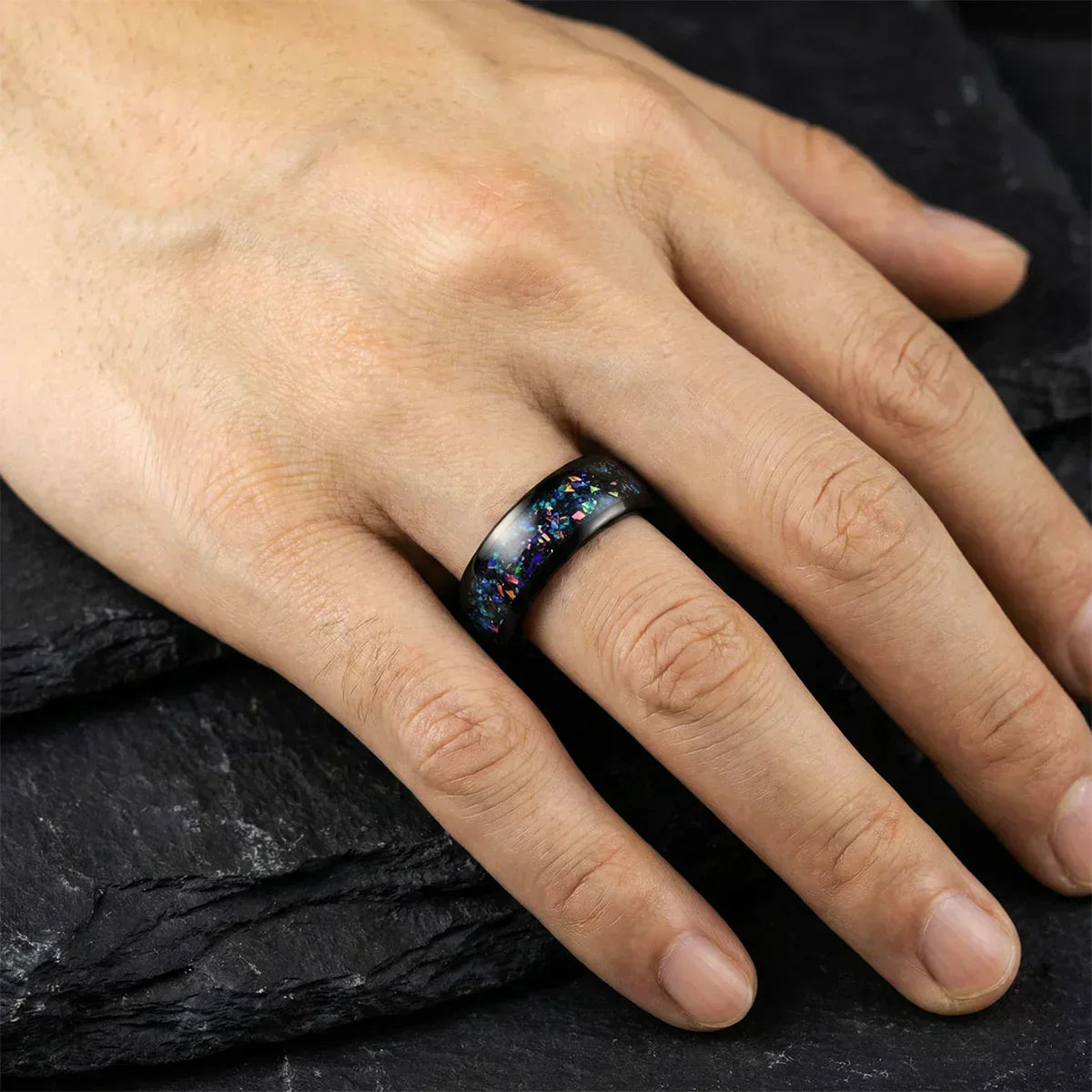 Anillo ancho de diseño moderno con incrustaciones coloridas en una mano sobre fondo oscuro