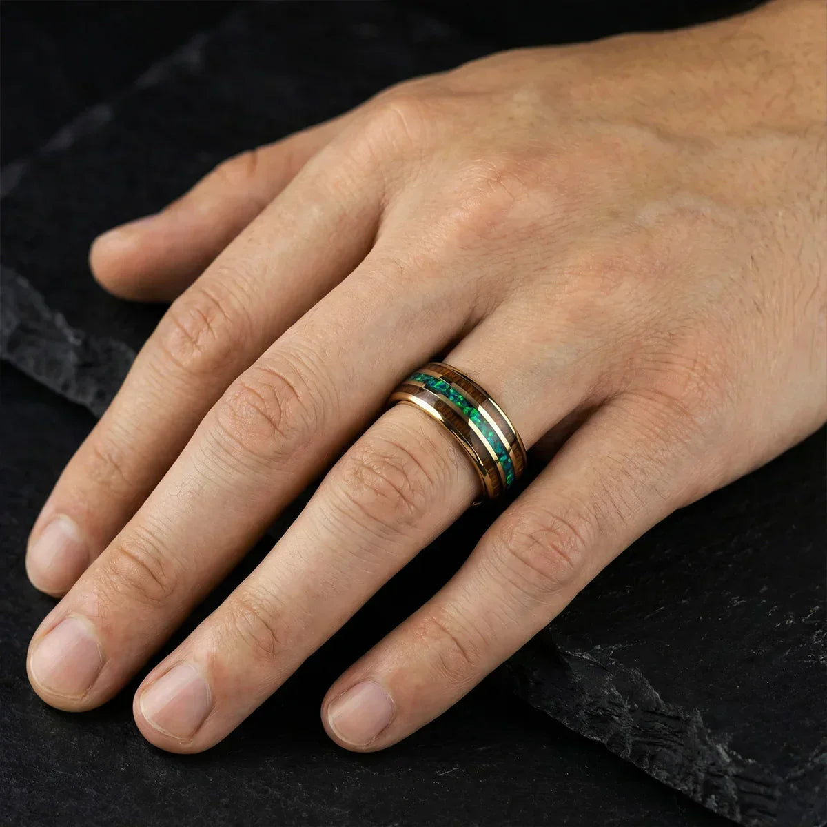 Mano masculina con anillo de lujo dorado y detalles verdes sobre fondo negro elegante