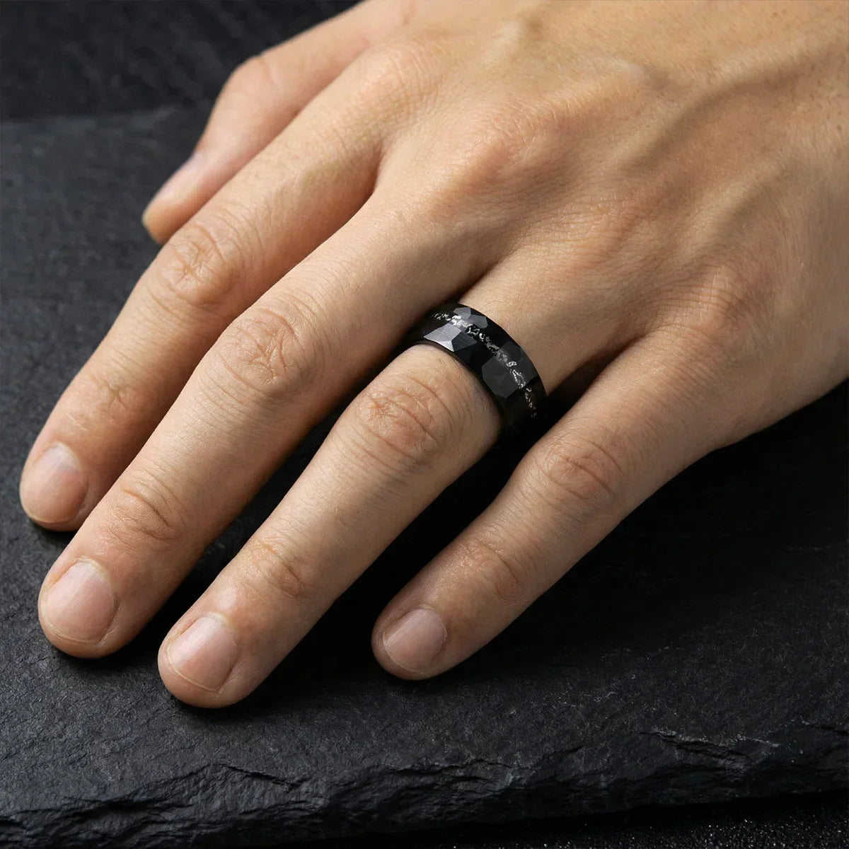 Anillo negro facetado para hombre en una mano sobre superficie oscura