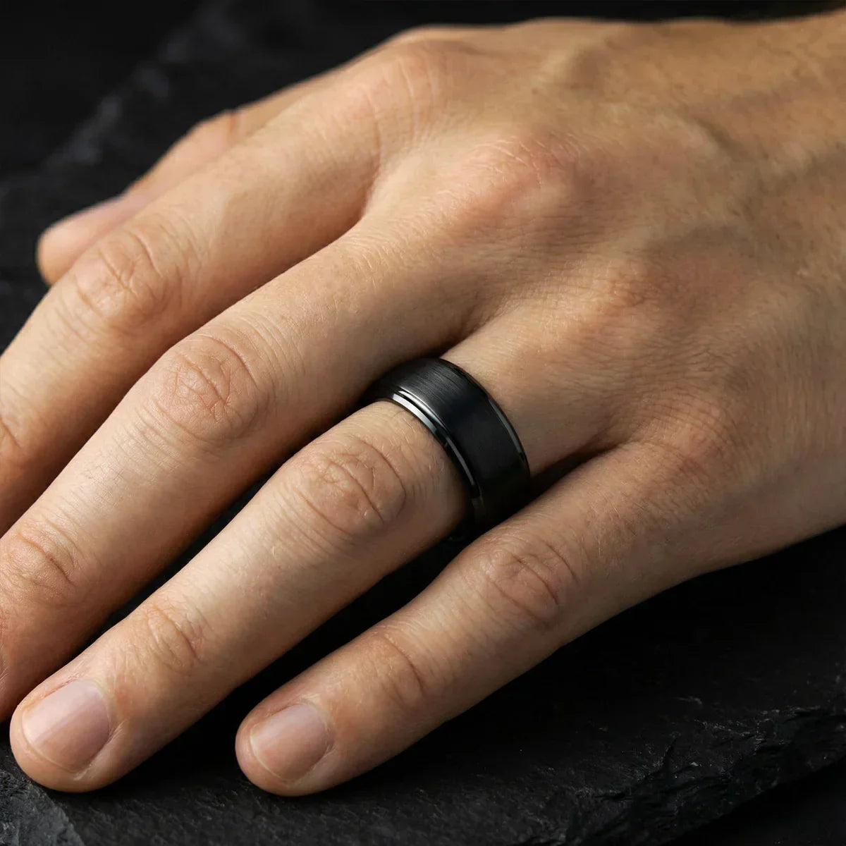 Anillo negro mate de acero en dedo masculino sobre fondo oscuro