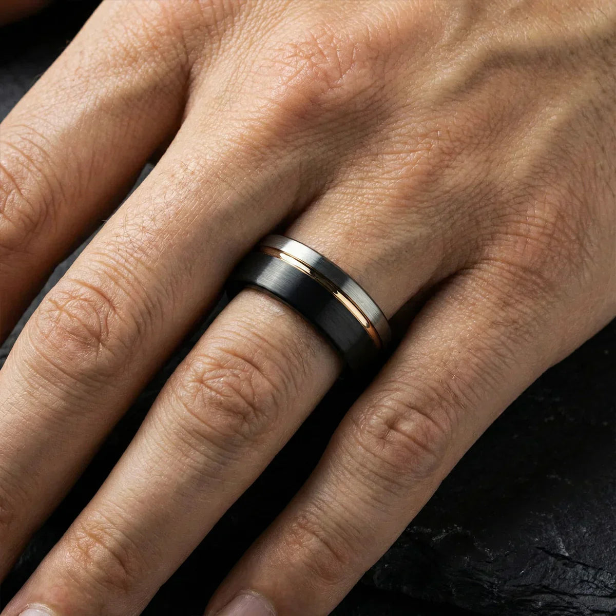 Anillo negro con detalles dorados en mano masculina, diseño moderno de joyería.