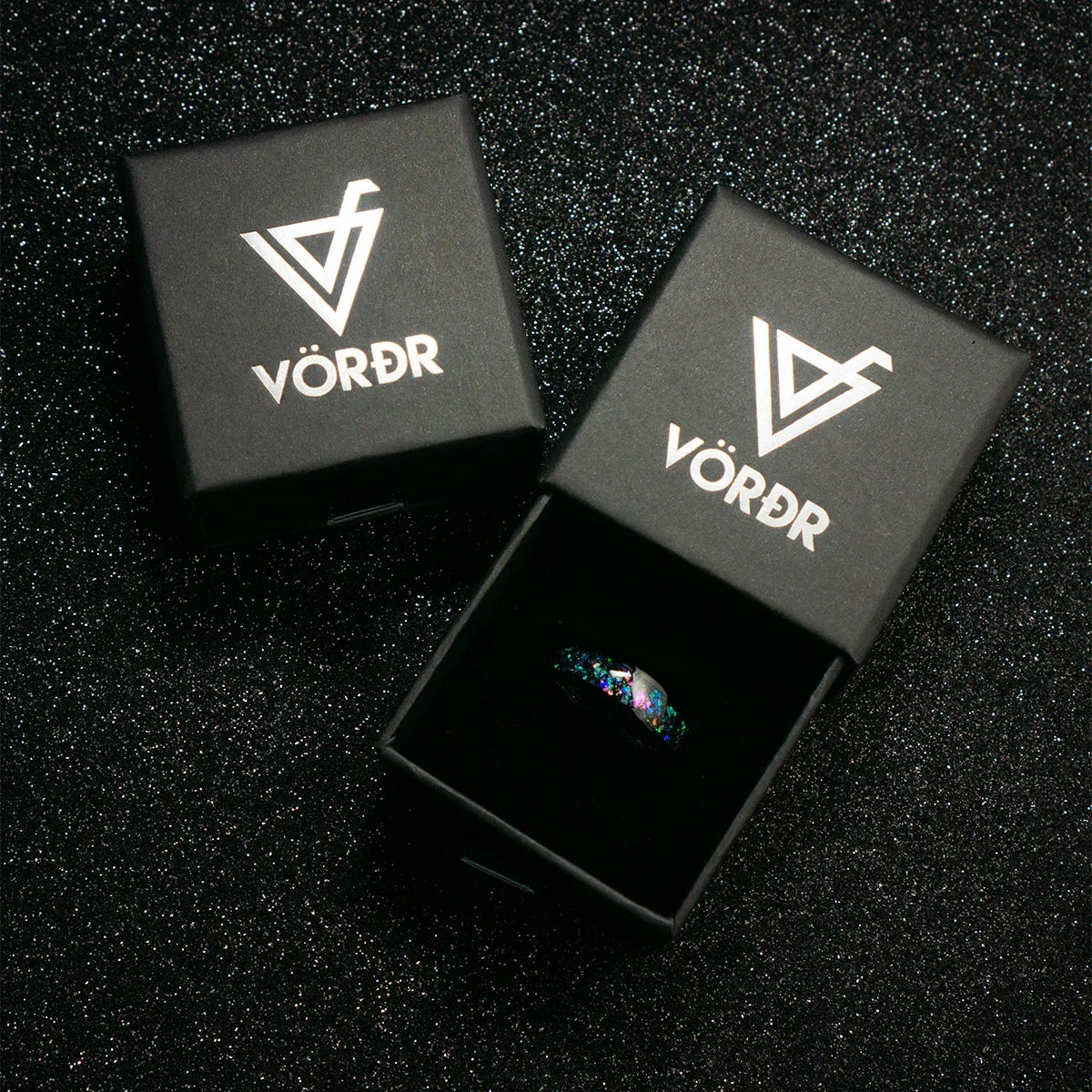 Anillo moderno con destellos coloridos en caja negra elegante sobre fondo brillante