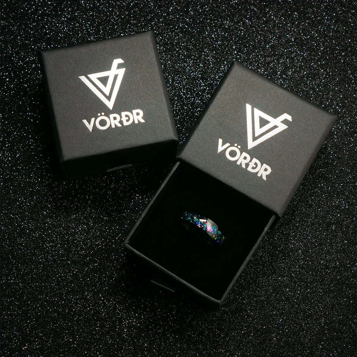 Anillo moderno con destellos coloridos en caja negra elegante sobre fondo brillante