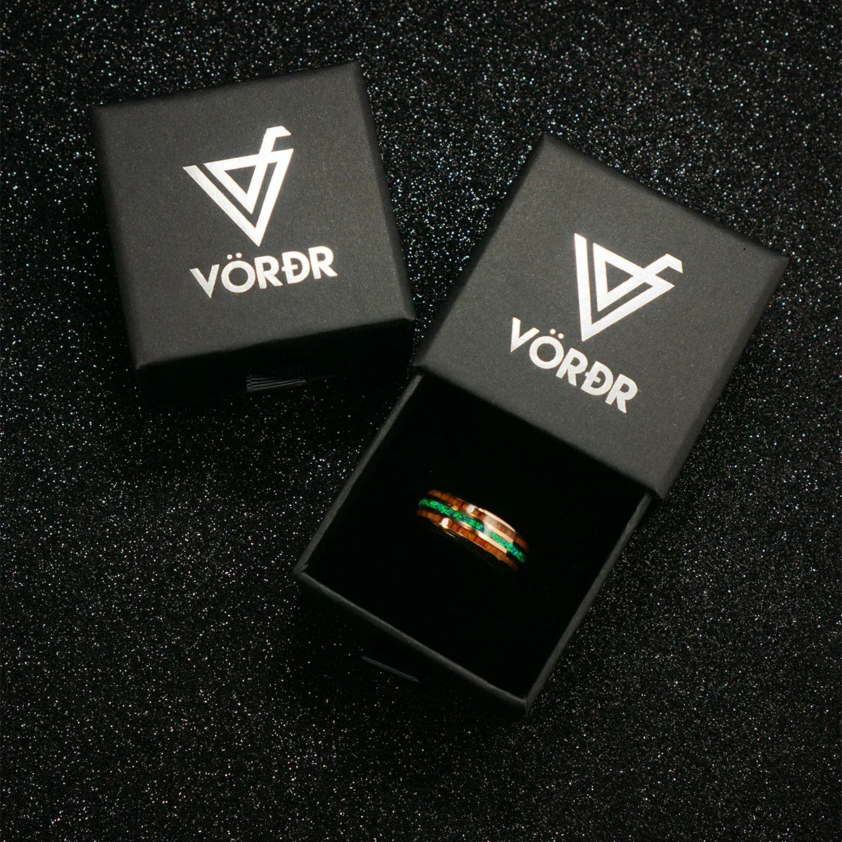 Anillo con detalles verdes y marrones en caja negra elegante sobre fondo brillante