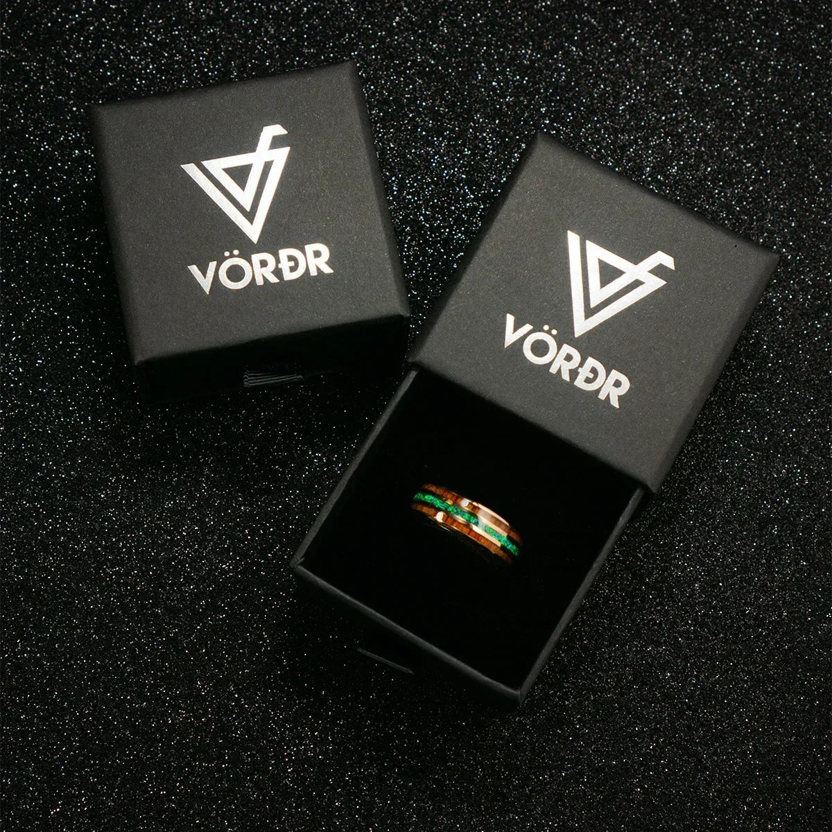 Anillo con detalles verdes y marrones en caja negra elegante sobre fondo brillante