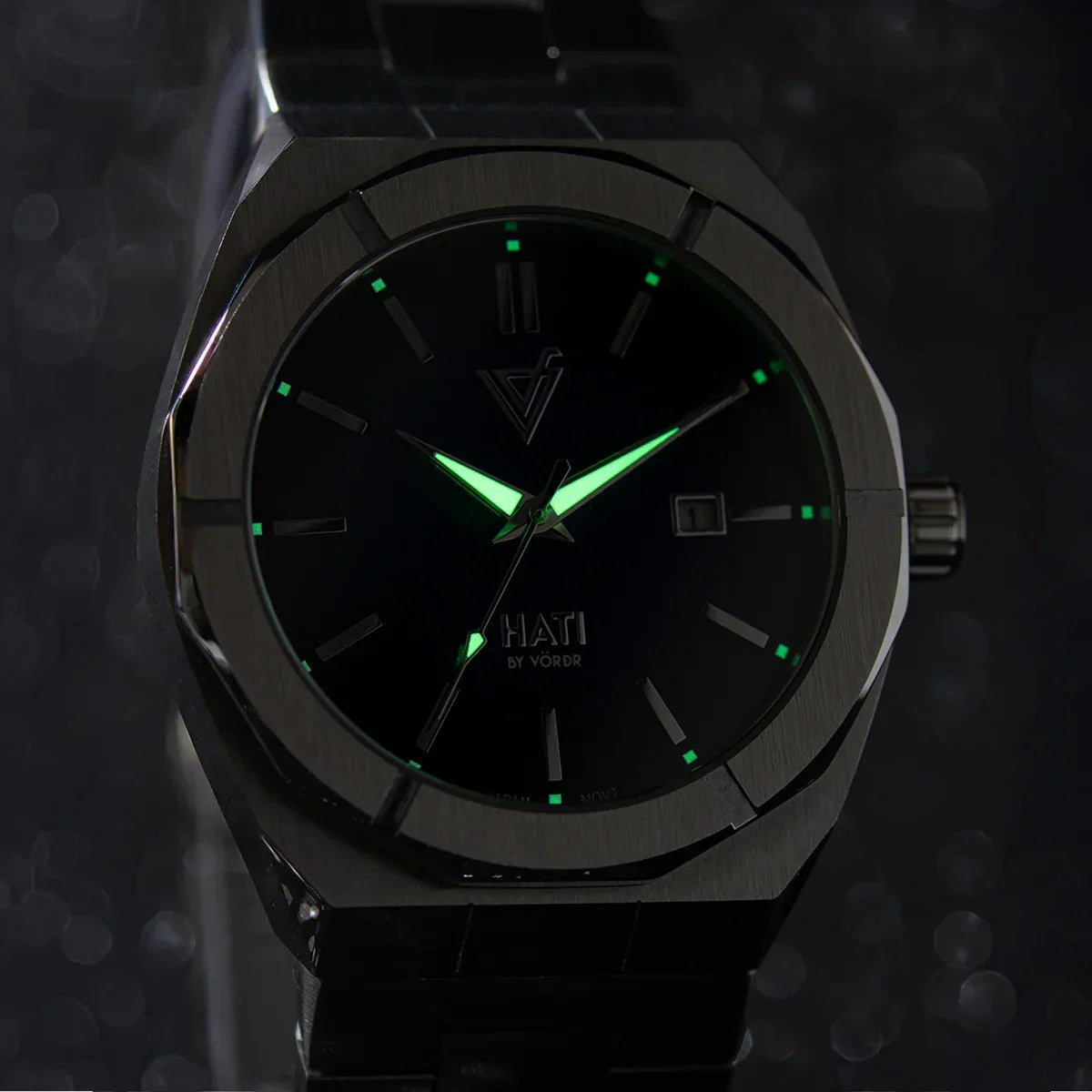 Reloj de pulsera negro con manecillas luminosas verdes y detalles minimalistas.