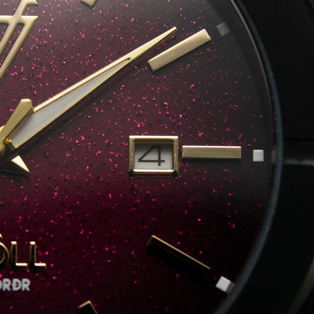 Detalle de reloj elegante con fondo burdeos brillante, manecillas y marcadores dorados, fechador visible.