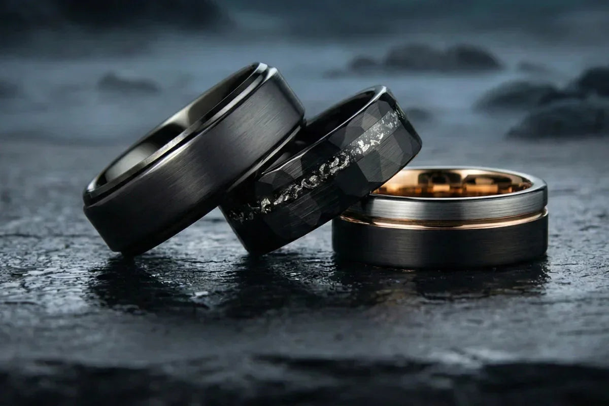 Anillos de tungsteno negros para hombre con acabados mate y detalles metálicos, sobre fondo oscuro.