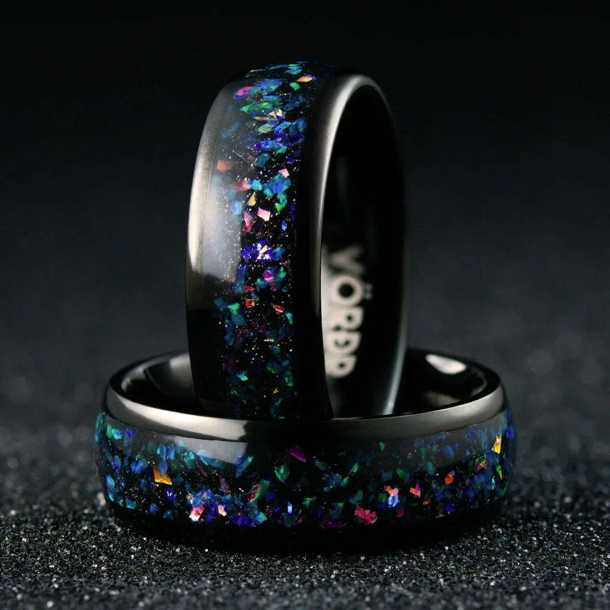 Anillo negro con incrustaciones brillantes multicolor sobre fondo oscuro, joyería moderna.