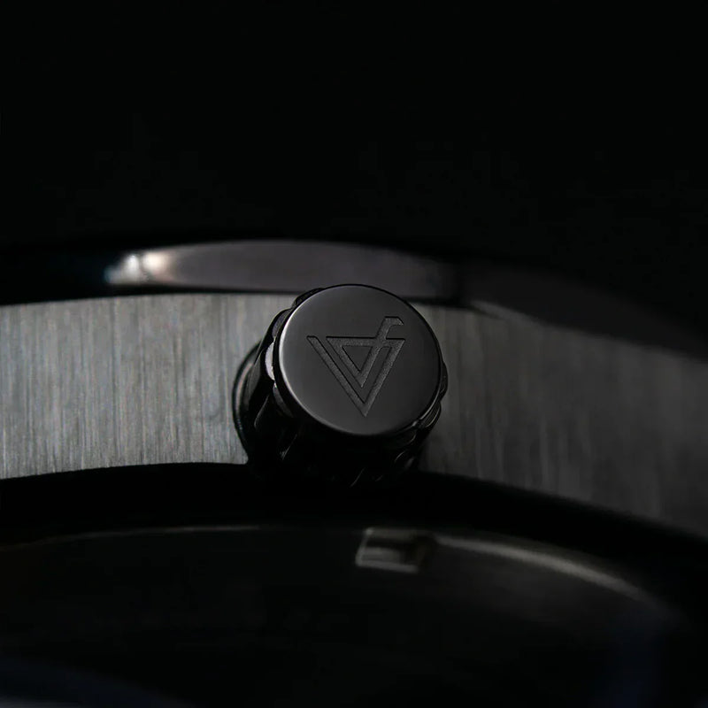 Detalle de la corona de un reloj metálico negro con logotipo grabado, estilo elegante.