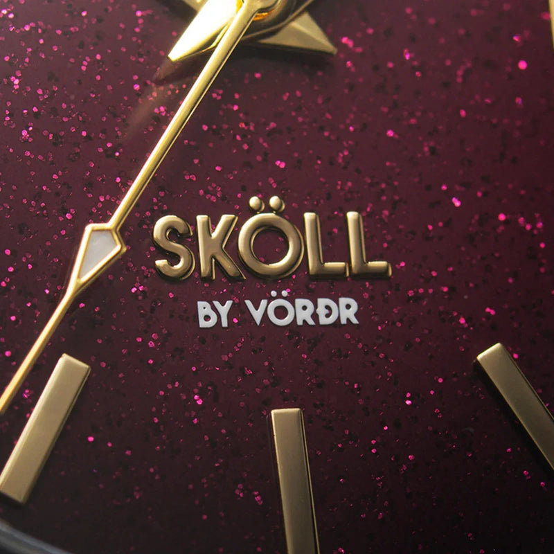 Reloj Sköll elegante con fondo burdeos brillante y detalles dorados, close-up de la carátula.